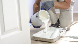 a professional painting contractor pouring white paint into a rolling tray